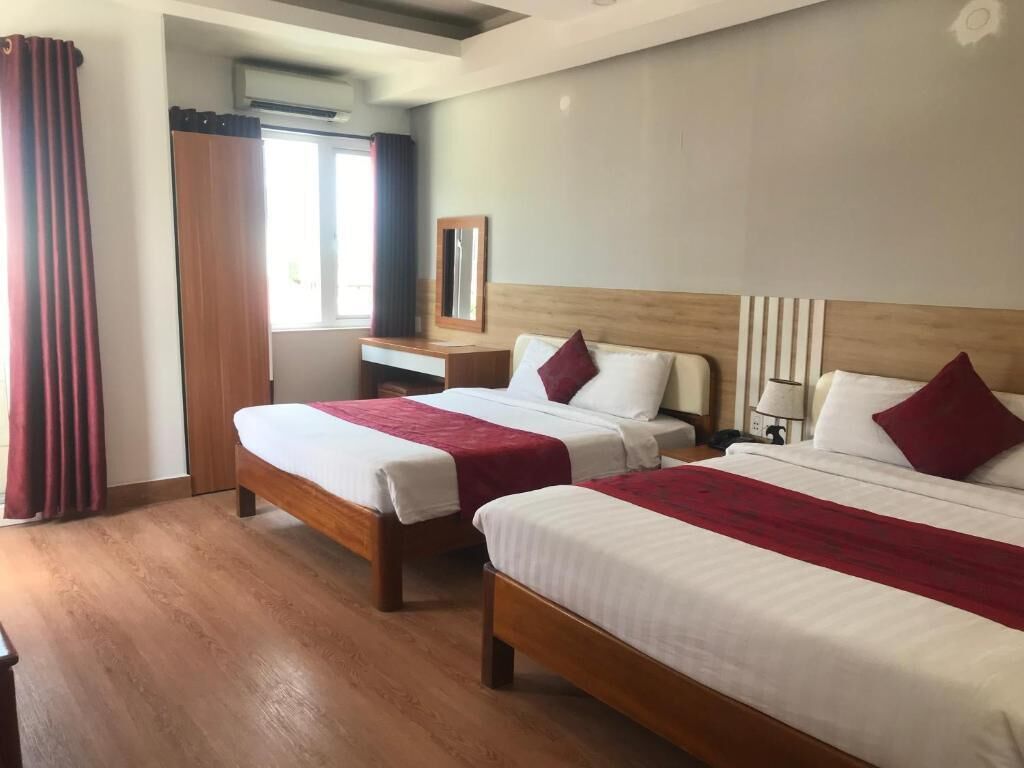 A hotel room with two beds, a wooden headboard, a desk, and a mirror.