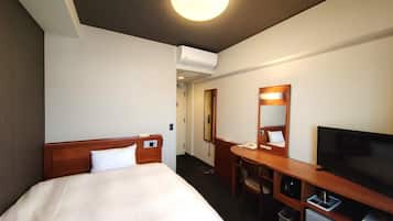 A hotel room with a bed, a desk, a chair, a television, and a small refrigerator.