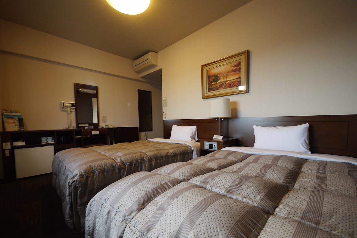 Hotellihuone, jossa on kaksi sänkyä, työpöytä, puhelin ja taulu seinällä.