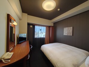 Habitación de hotel con cama, escritorio con teléfono, televisor, ventana con cortinas y una lámpara en el techo.