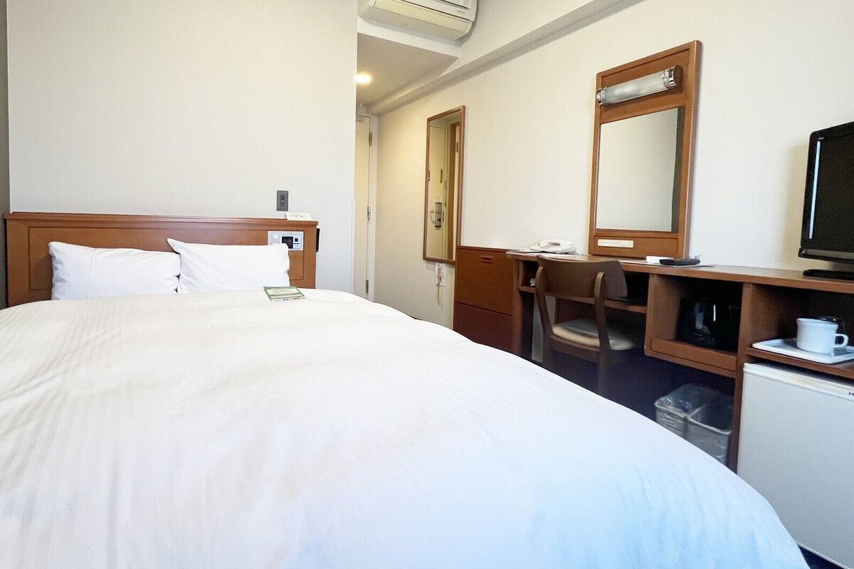 Hotellihuone, jossa on suuri sänky, työpöytä tuolilla, televisio ja peili.