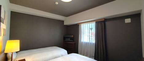 Habitación de hotel con dos camas, una mesita de noche con lámpara, televisión y ventana con cortinas.