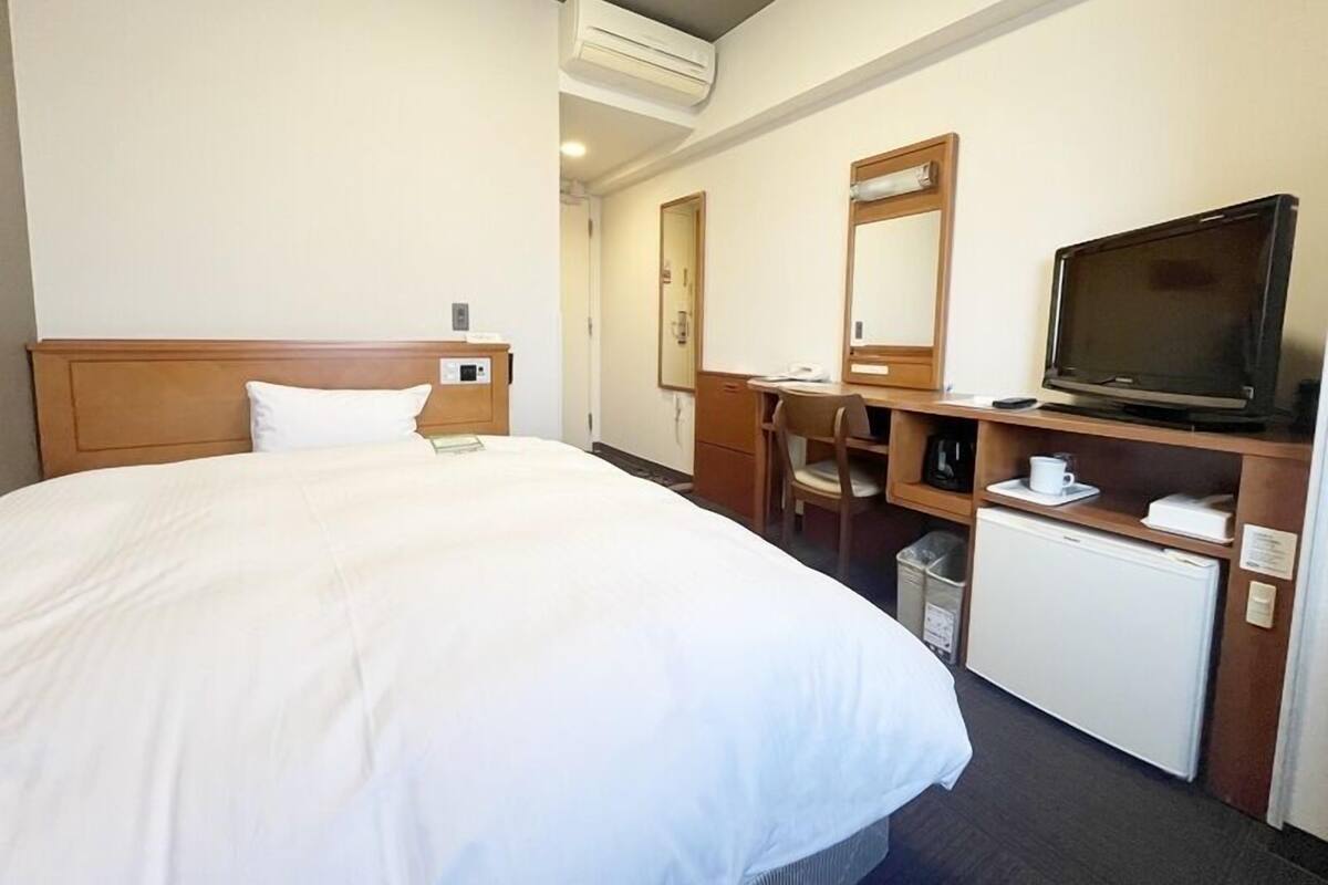 Hotellihuone, jossa on suuri sänky, työpöytä tuolilla, televisio ja pieni jääkaappi.