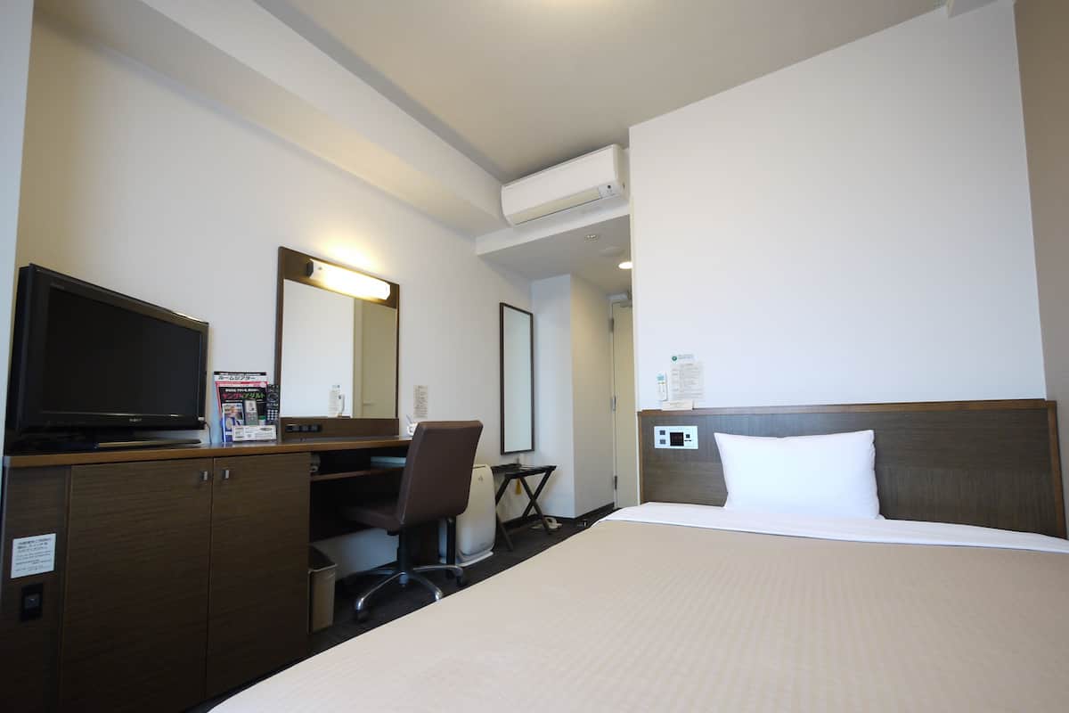 Una habitación de hotel con cama, escritorio con computadora, televisor y aire acondicionado.