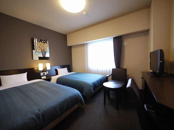 A hotel room with two beds, a desk with a chair, a television, and a window with curtains.