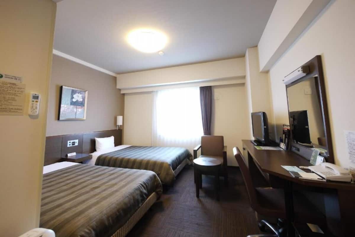 Habitación de hotel con dos camas, un escritorio con computadora, una silla y un televisor.