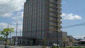 A multi-story hotel with a green sign at the top, a flat facade, and a parking area in front. - Hotel Route Inn Ishinomaki Kanan Inter (Isinomaki)