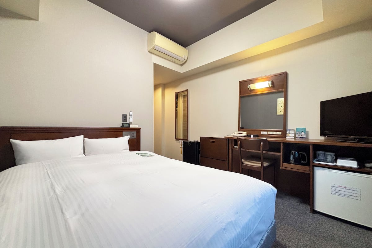 A hotel room with a large bed, a desk, a chair, a television, and a minibar.