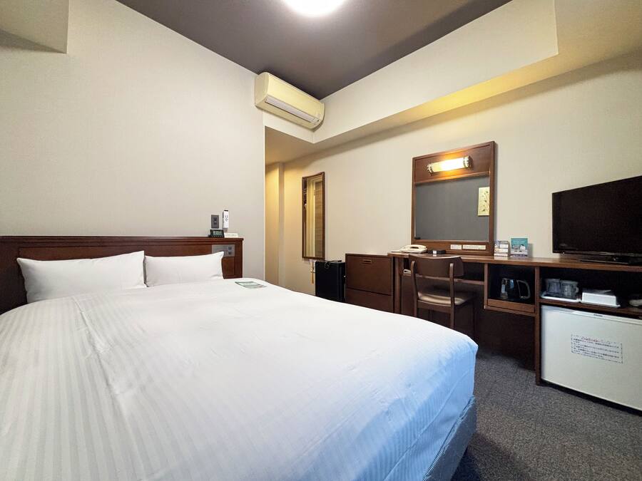 A hotel room with a large bed, a desk, a chair, a television, and a minibar.