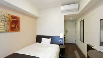 A hotel room with a bed, bedside table, and a wall-mounted air conditioner.