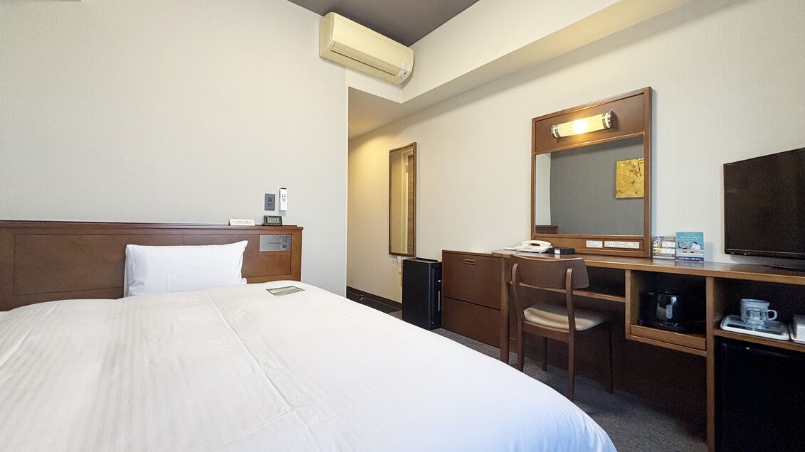 Een hotelkamer met een bed, een bureau, een stoel, een televisie, een spiegel en een koffiezetapparaat.