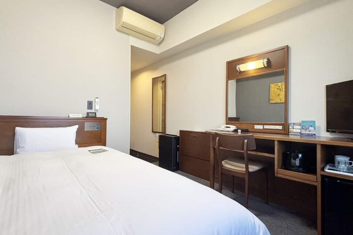 A hotel room with a bed, a desk, a chair, a television, a mirror, and a coffee machine.