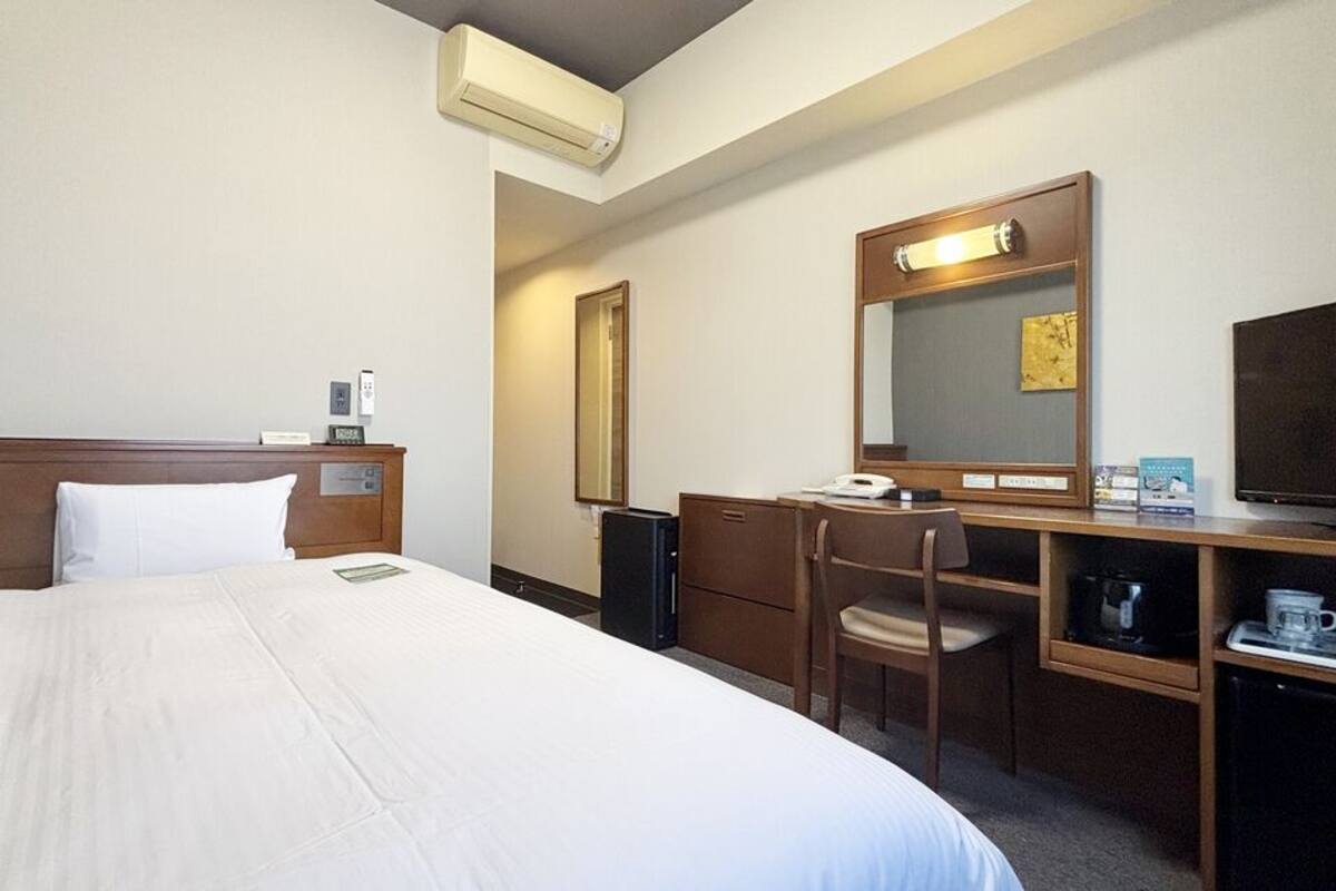 A hotel room with a bed, a desk, a chair, a television, a mirror, and a coffee machine.