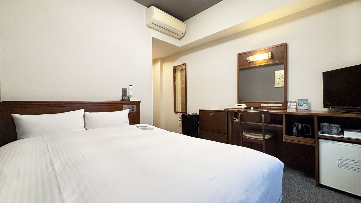 Een hotelkamer met een groot bed, een bureau met stoel, een televisie, een spiegel en een kleine koelkast.