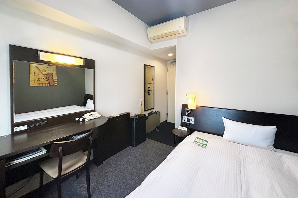 A hotel room with a bed, desk, chair, and a large mirror.