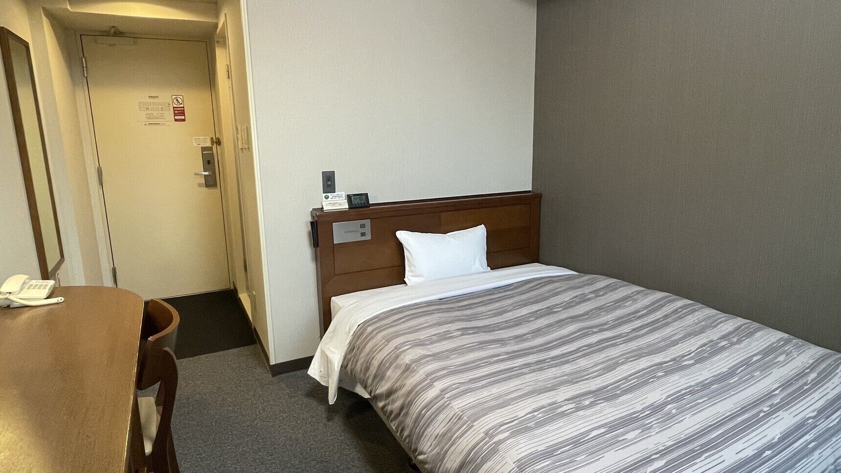 Quarto de hotel com cama, escrivaninha, telefone e porta.