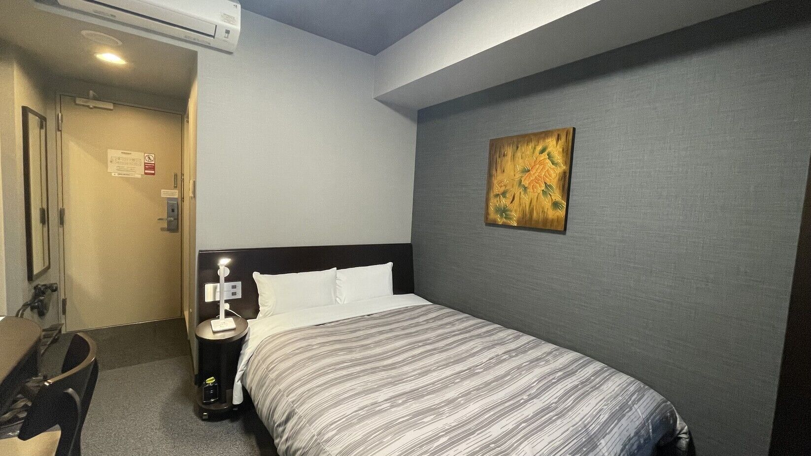 Quarto de hotel com cama, mesa de cabeceira, abajur e um quadro na parede.