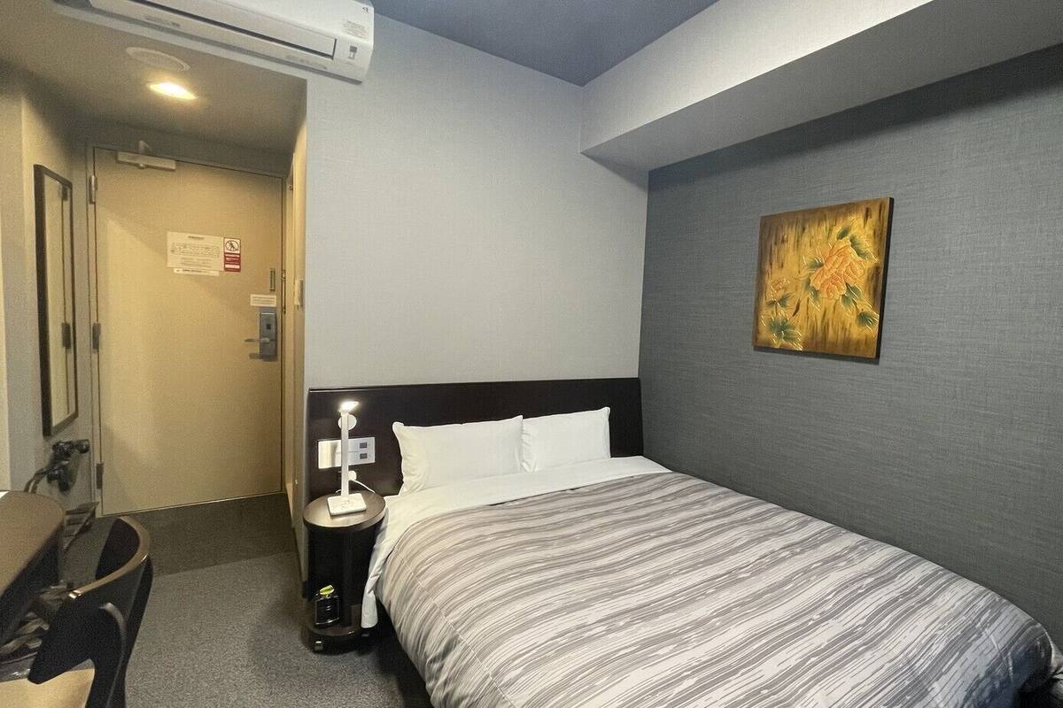 Quarto de hotel com cama, mesa de cabeceira, abajur e um quadro na parede.