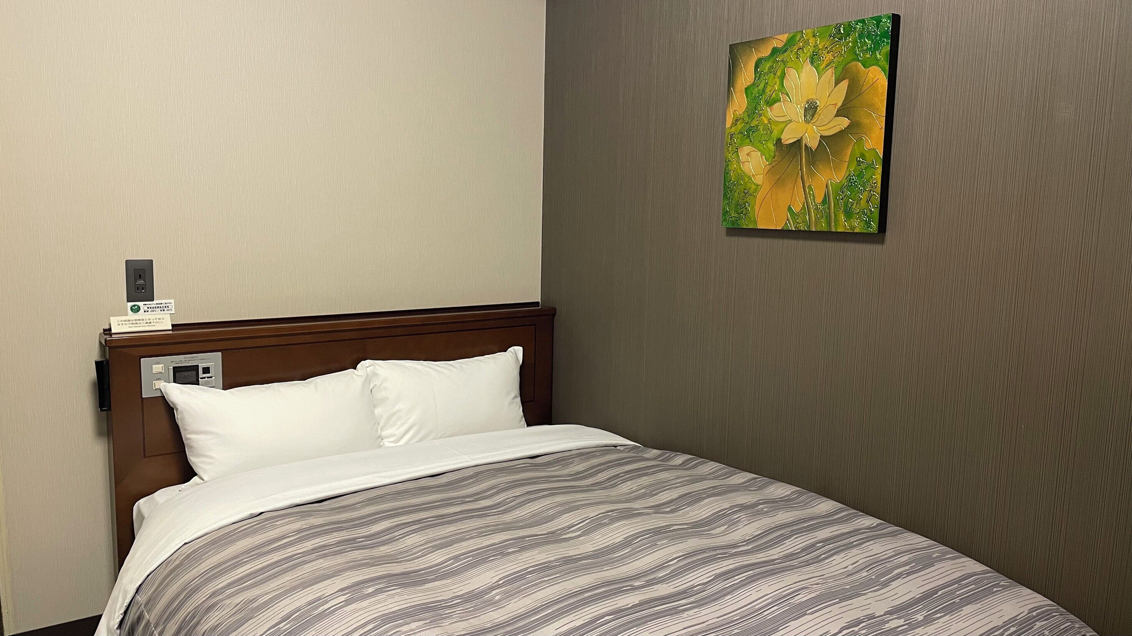 Quarto de hotel com cama, cabeceira, obra de arte na parede e painel de controle.
