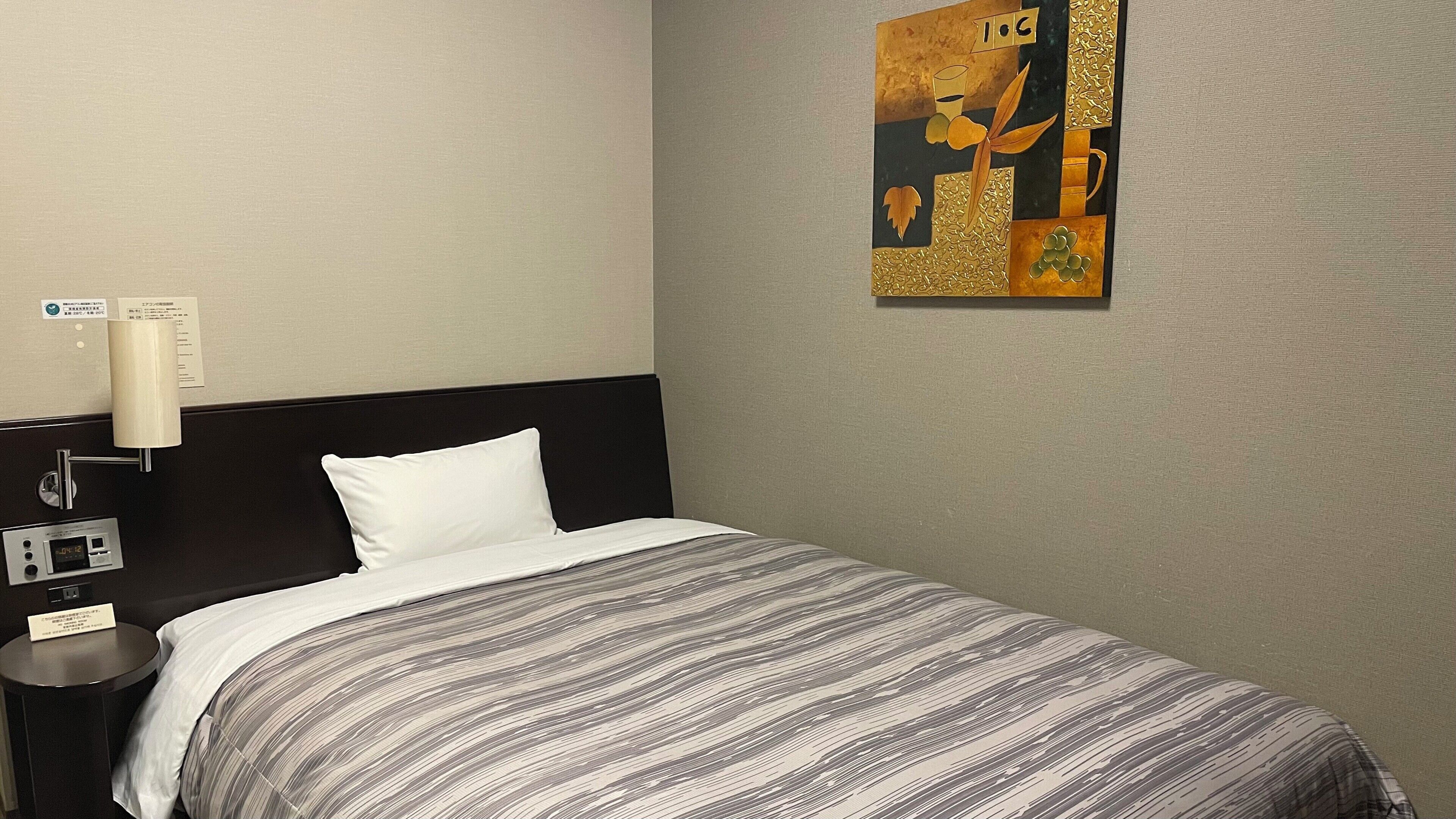 Quarto de hotel com uma cama, mesa de cabeceira, luminária na parede e um quadro.