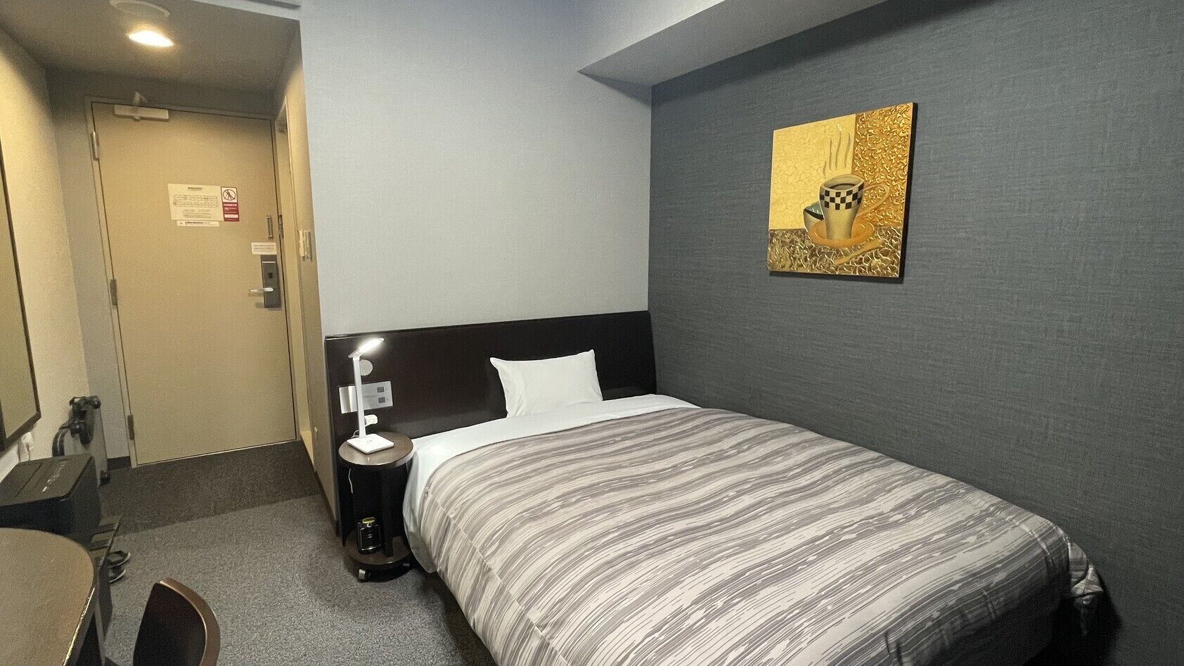 Quarto de hotel com cama, mesa de cabeceira, abajur e um quadro na parede.