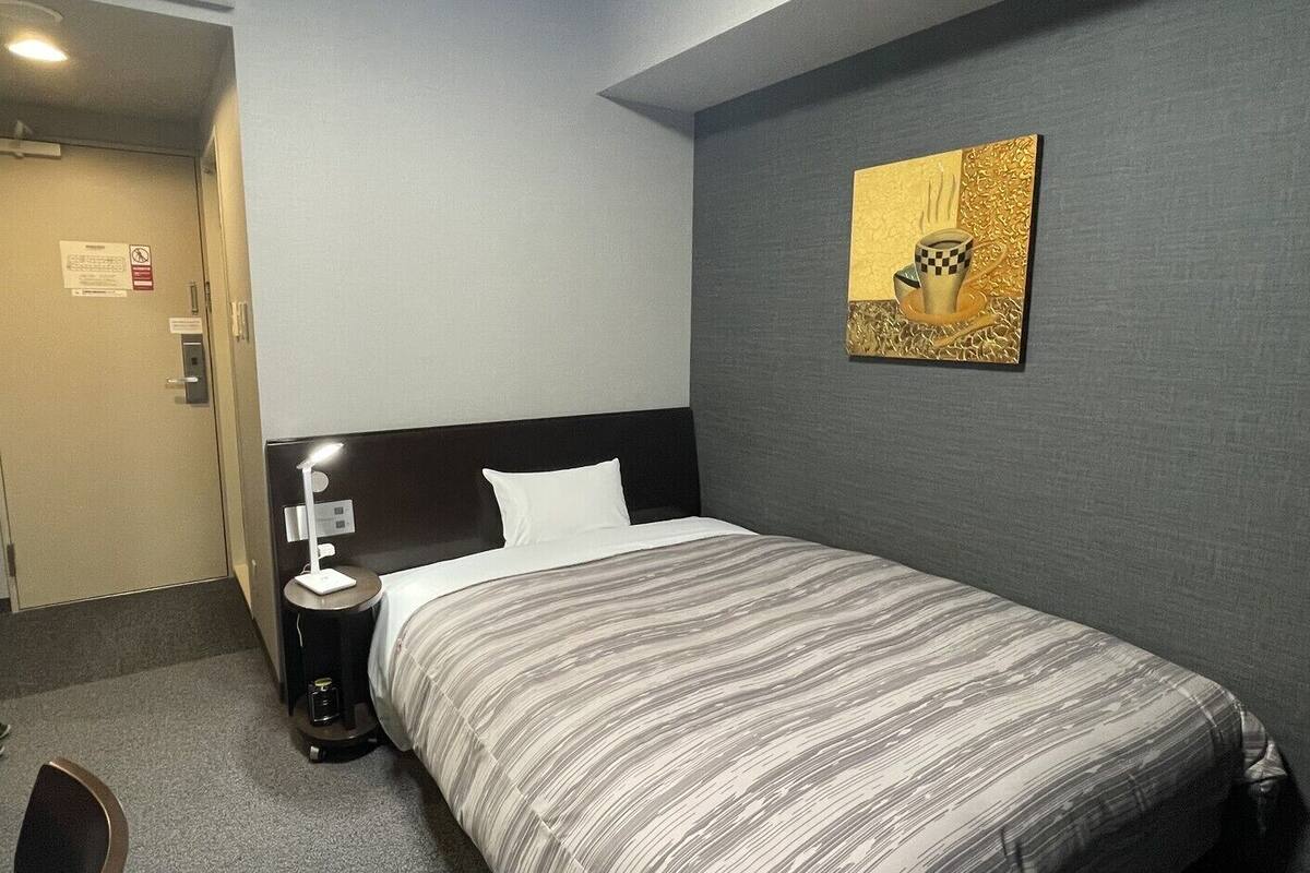 Quarto de hotel com cama, mesa de cabeceira, abajur e um quadro na parede.