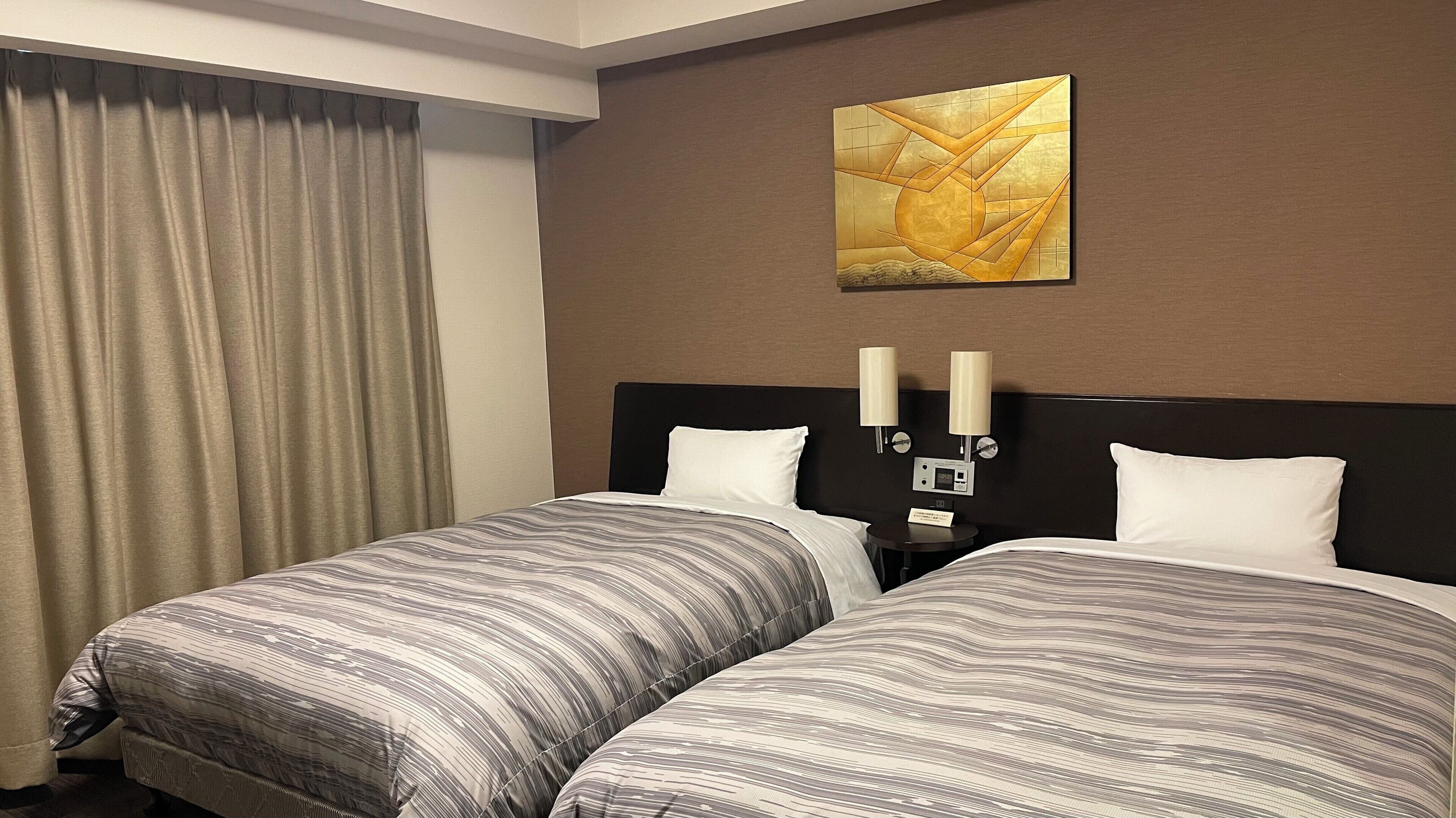 Quarto de hotel com duas camas, uma janela grande com cortinas, uma obra de arte na parede e luminárias de cabeceira.