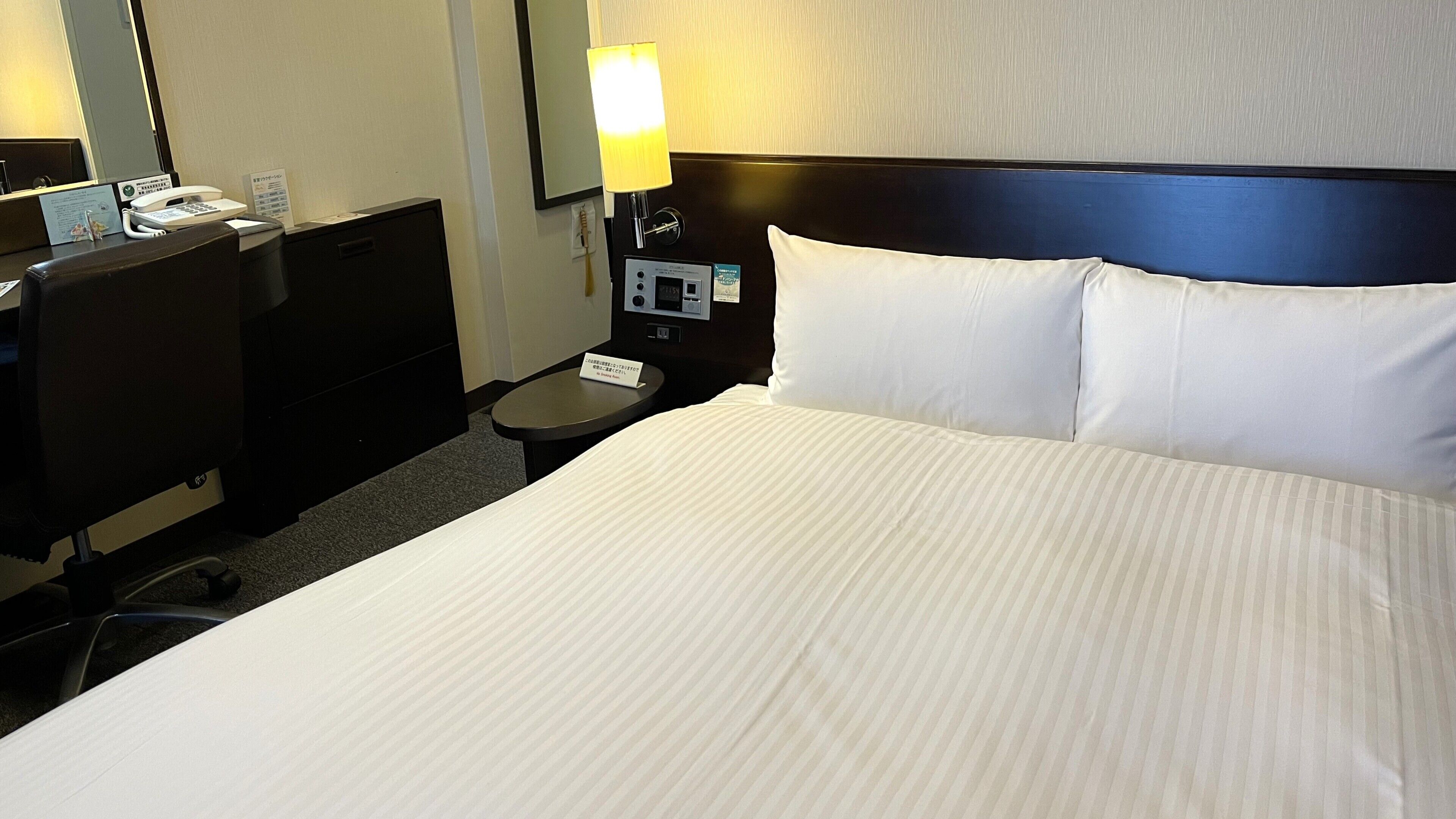 Et hotelværelse med seng, skrivebord, telefon, lampe og et natbord.