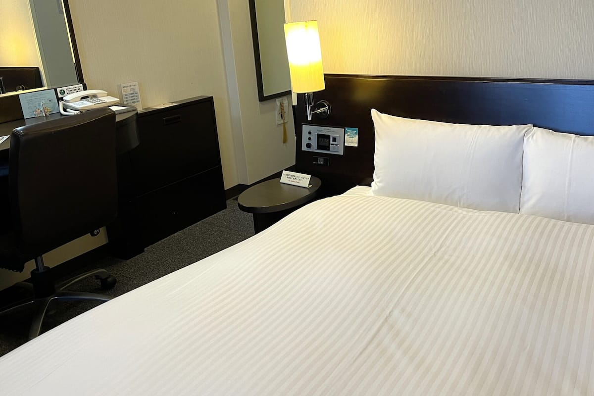 A hotel room with a bed, a desk, a telephone, a lamp, and a nightstand.