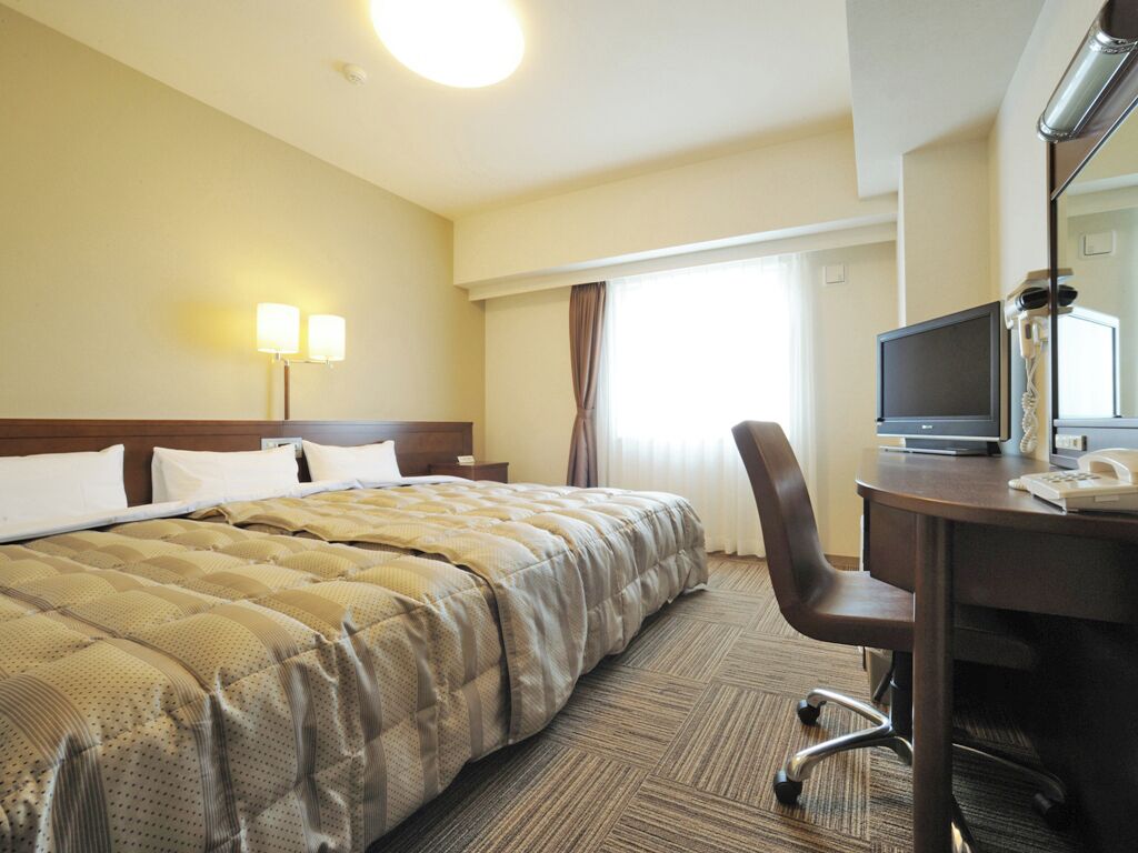 A hotel room with a large bed, a desk with a computer, and a TV.