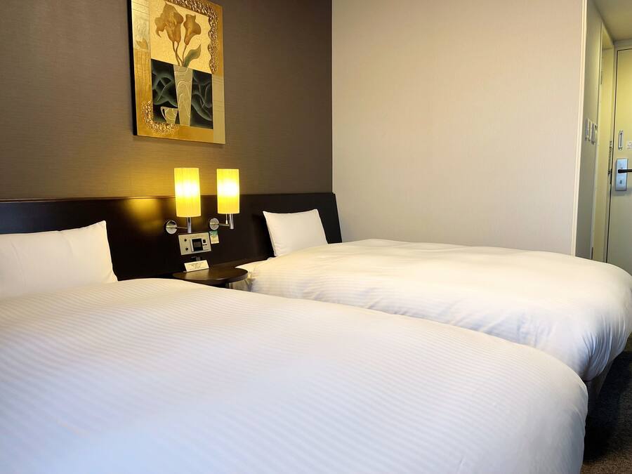 A hotel room with two beds, a nightstand with a lamp, and a wall-mounted artwork.