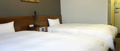 Habitación de hotel con dos camas, una mesita de noche con lámpara, un cuadro en la pared y una puerta a la derecha.