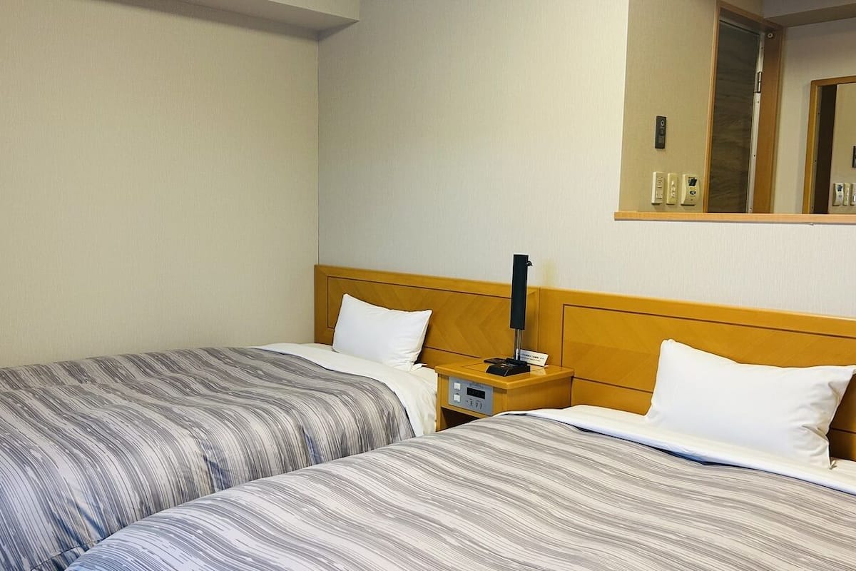 Ein Hotelzimmer mit zwei Betten, einem Nachttisch mit Lampe, einem Spiegel und einer Wandsteckdose.