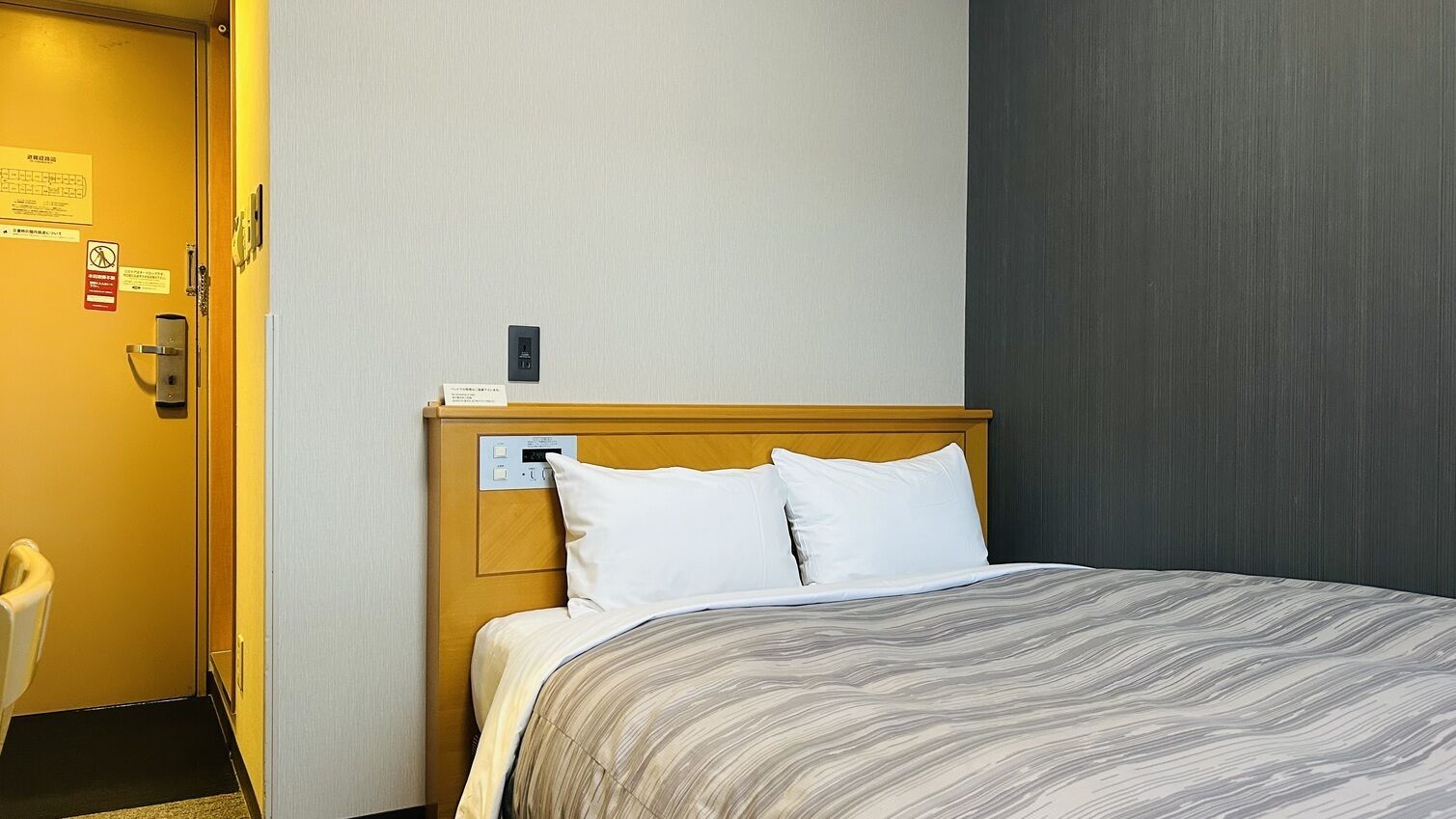 A hotel room with a bed, a wooden headboard, a control panel, and a door with a sign.
