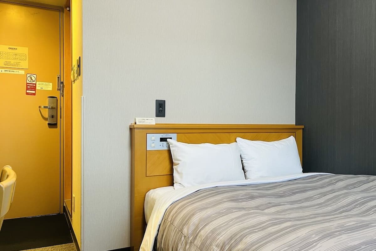 Ein Hotelzimmer mit einem Bett, einem Holzkopfende, einer Bedienkonsole und einer Tür mit einem Schild.