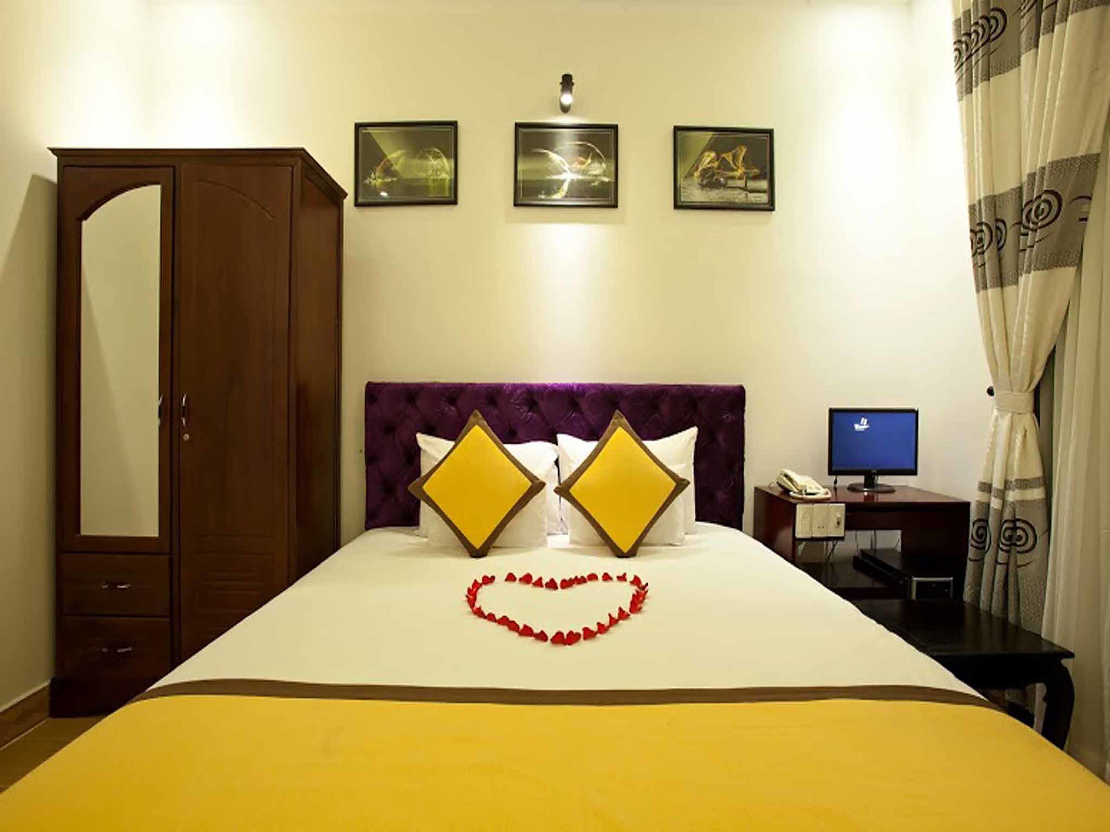 A hotel room with a bed, a desk with a computer, a wardrobe, and three framed pictures on the wall.