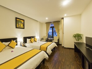 Une chambre d’hôtel avec deux lits, un bureau, une chaise, une petite table, une plante en pot et une fenêtre avec des rideaux.