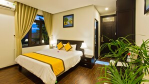 Habitación de hotel con cama, lámparas de noche, mesita de noche, planta en maceta y una puerta.