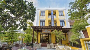 Un hotel con fachada amarilla, zona de estar exterior con muebles de mimbre y un letrero que dice "HAI AU Boutique Hotel".