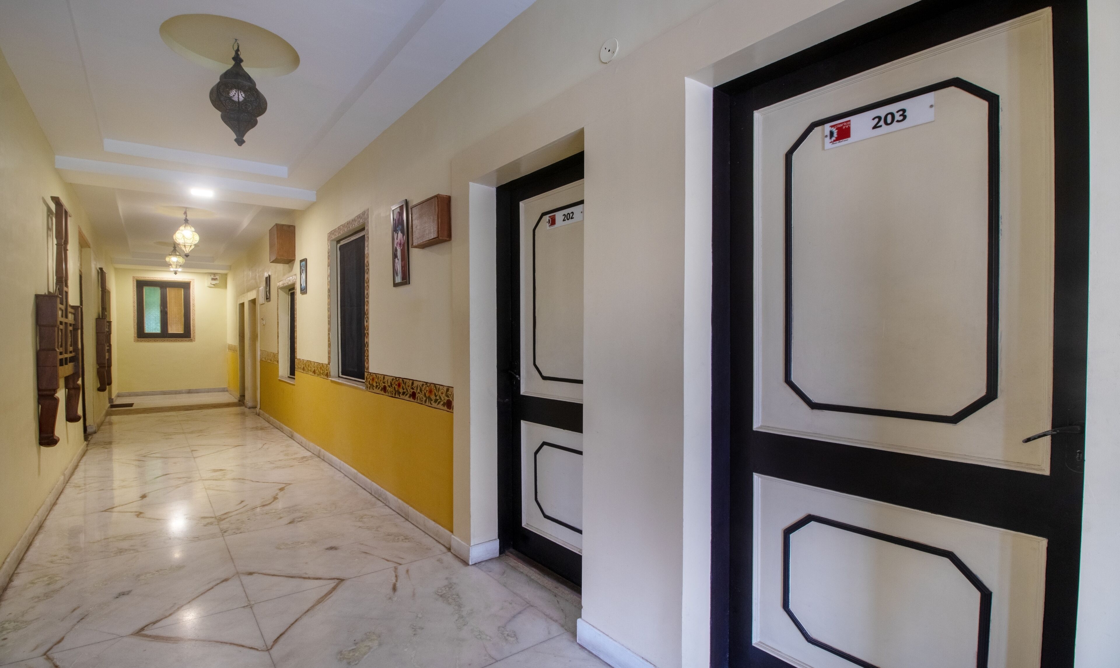 A hallway with a marble floor, doors numbered 202 and 203, and a ceiling light fixture.