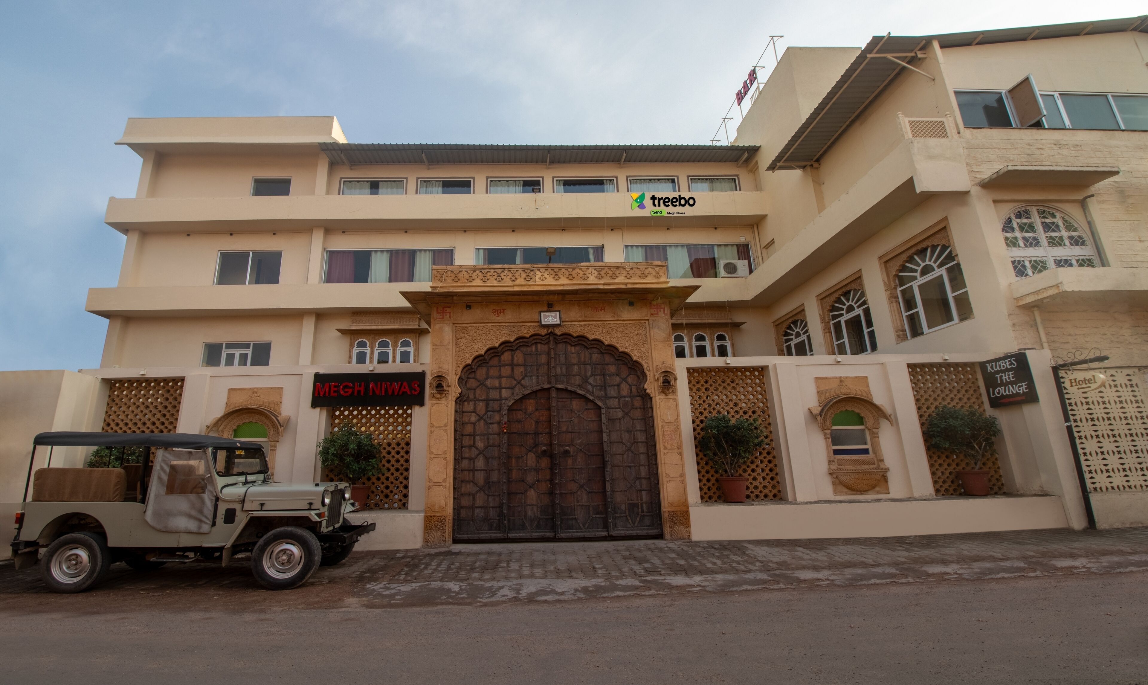 Un hôtel doté d’une entrée de style traditionnel, d’une enseigne indiquant « MEGH NIWAS » et d’une autre indiquant « KUBES THE LOUNGE ».
