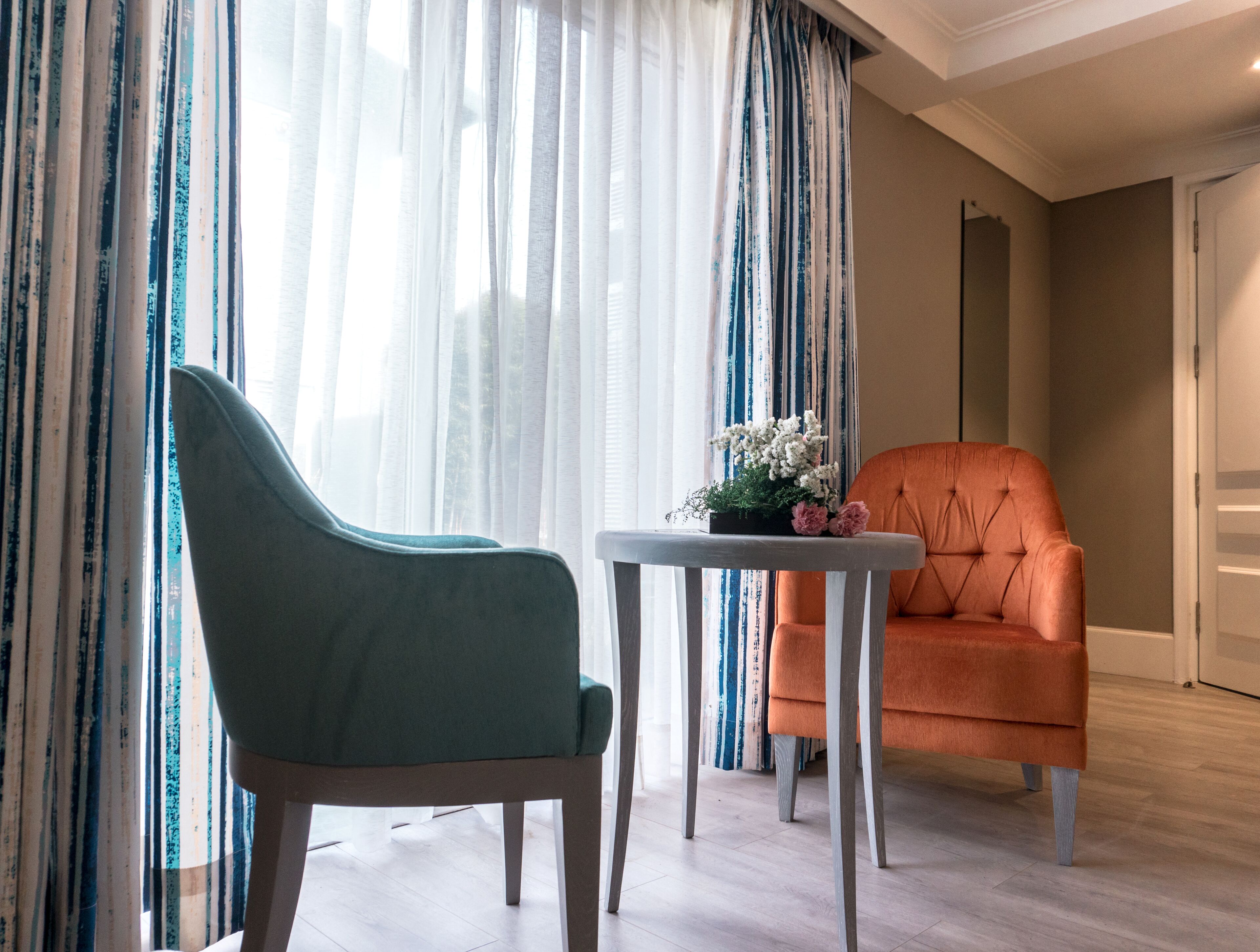 Una habitación con un sillón verde azulado, un sillón naranja y una pequeña mesa con un arreglo floral.