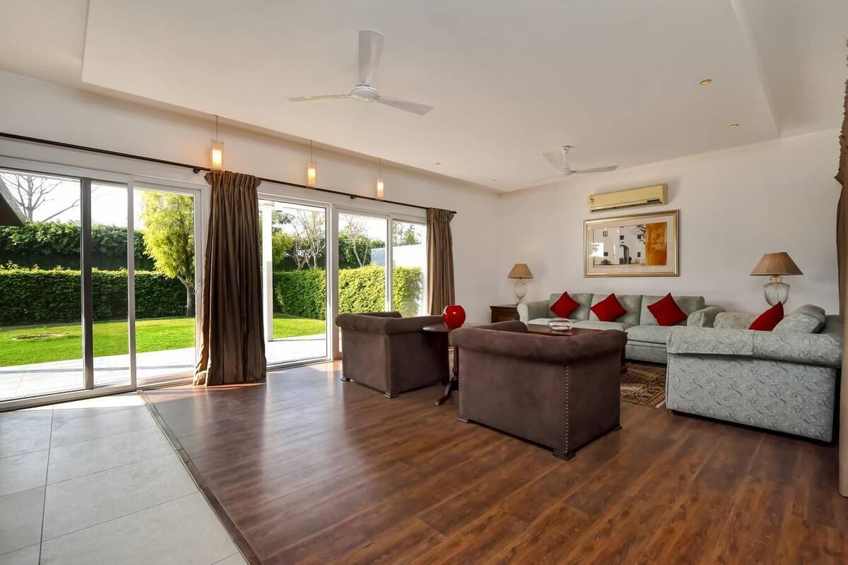 A spacious living room with a large sliding glass door leading to a garden, a sofa set, and a coffee table.