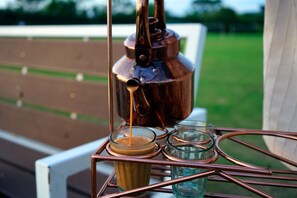 A copper kettle pouring coffee into a glass on a metal table. - Amatra By the Ganges (Haridwar)