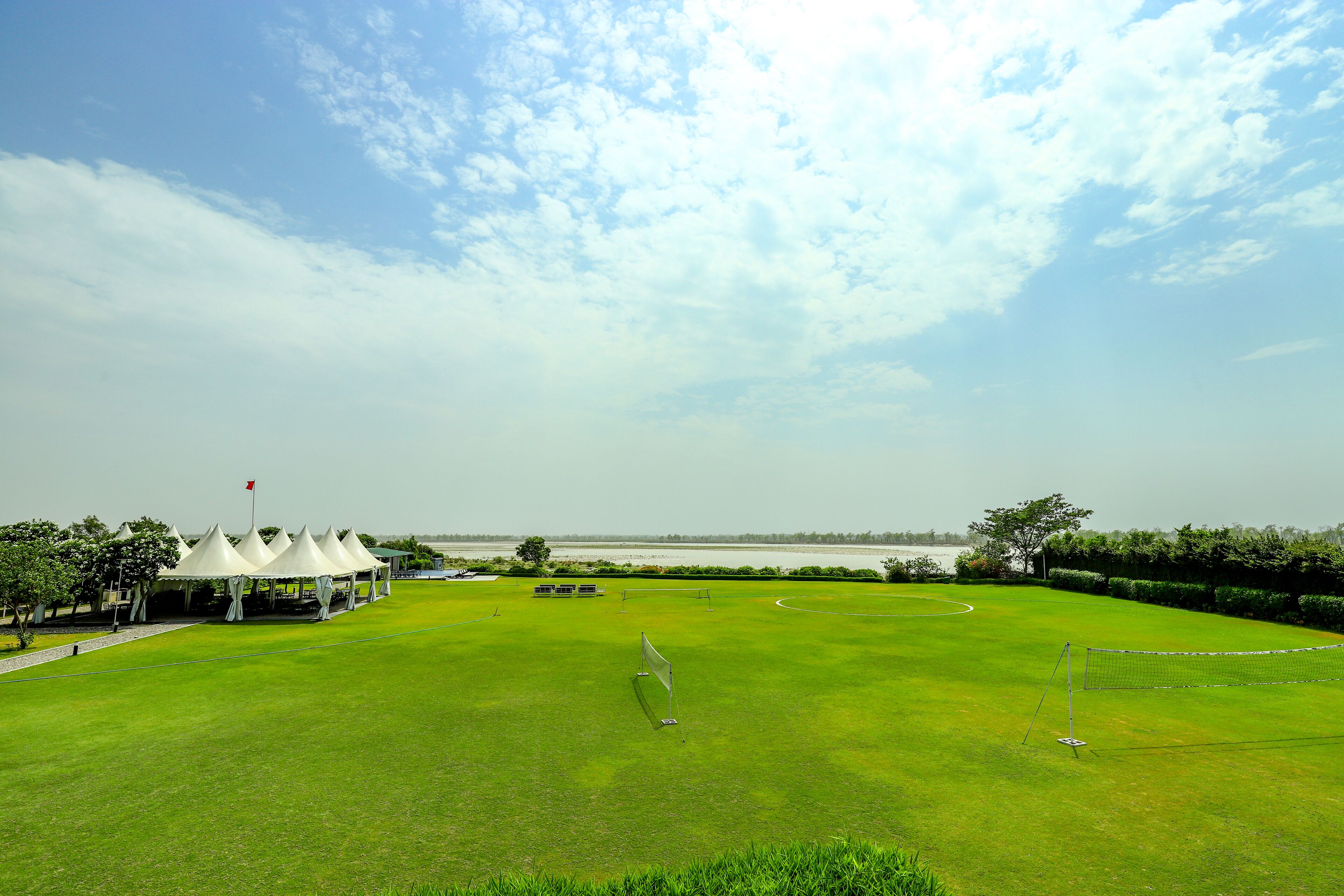 A golf course with tents, a netted area, and a view of the water in the distance.