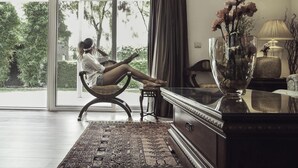 A room with a large sliding glass door leading to a garden, a sofa, a table, and a decorative vase with flowers.