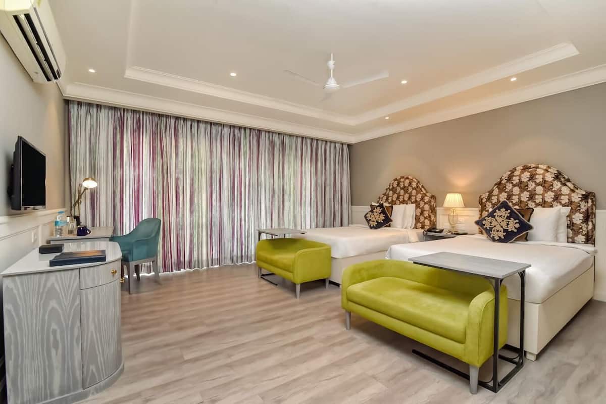 A hotel room with two beds, a desk, a chair, and a television.