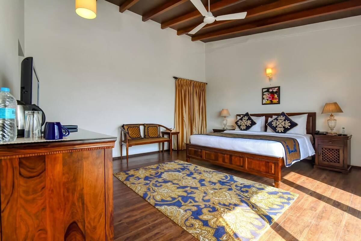 A hotel room with a wooden bed, a desk with a computer, a chair, a patterned rug, and a ceiling fan.