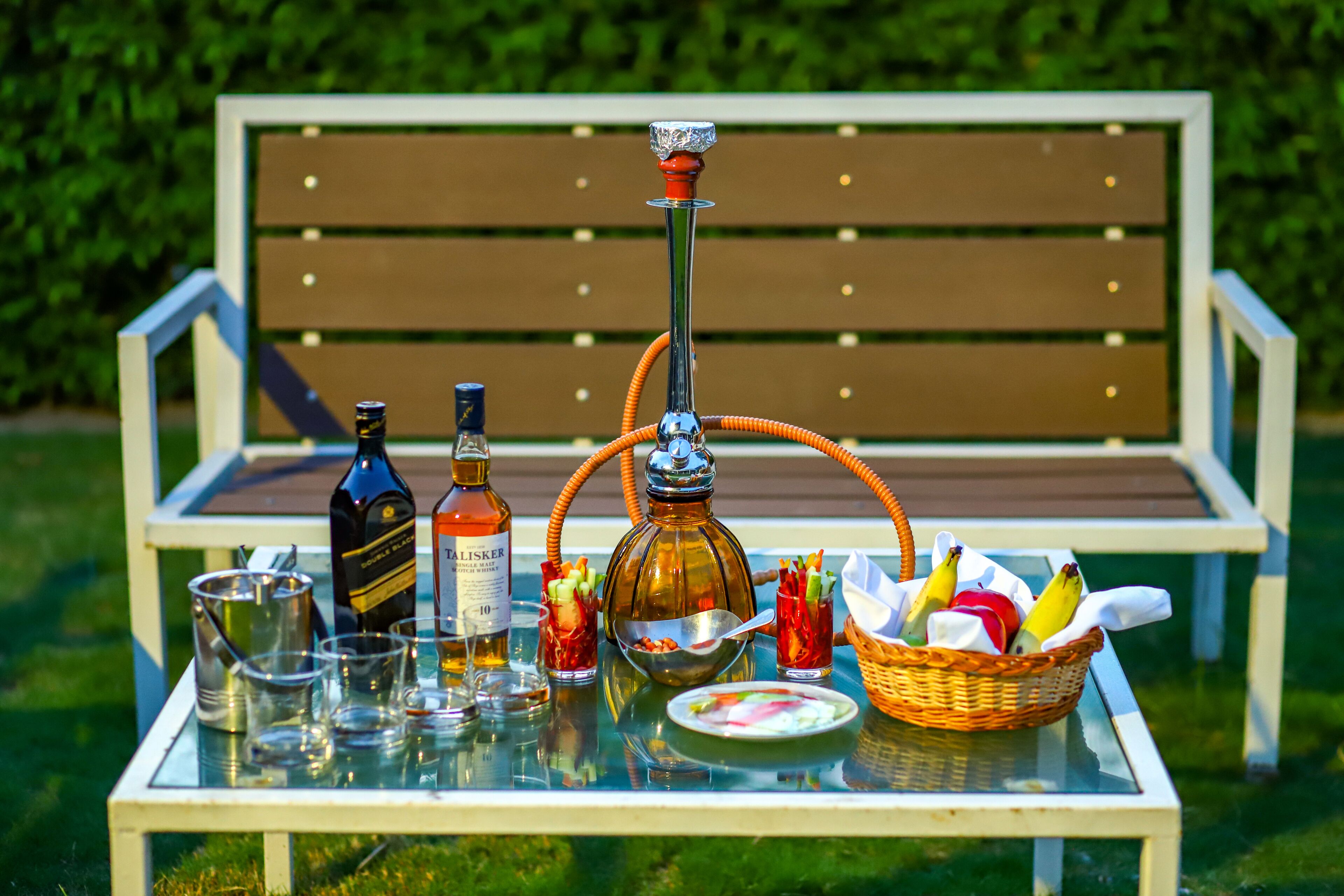 Une table en verre avec un narguilé, des bouteilles, des verres et un panier de fruits.