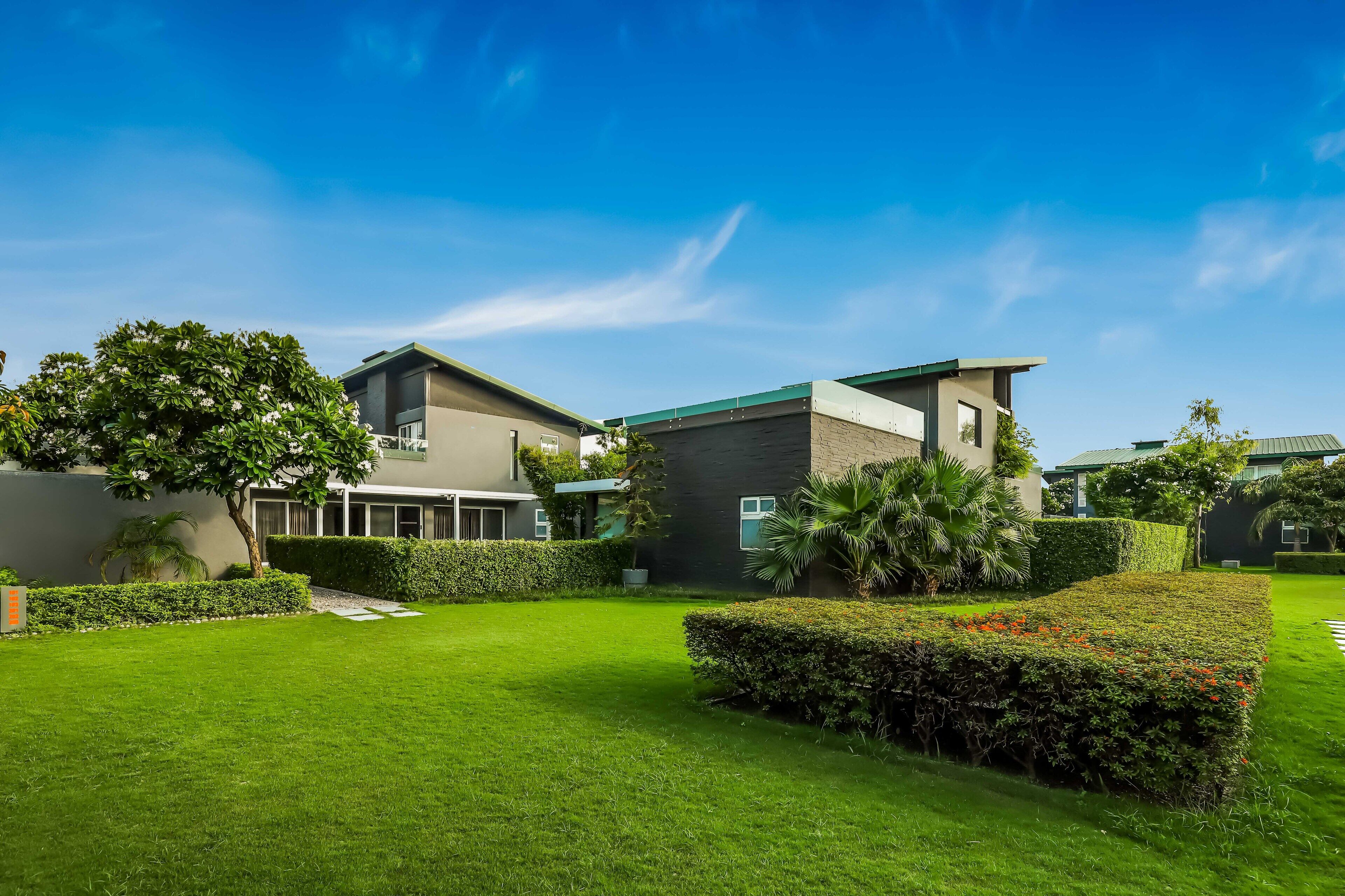 A modern residential area with well-maintained lawns and hedges, featuring contemporary houses with large windows and flat roofs.